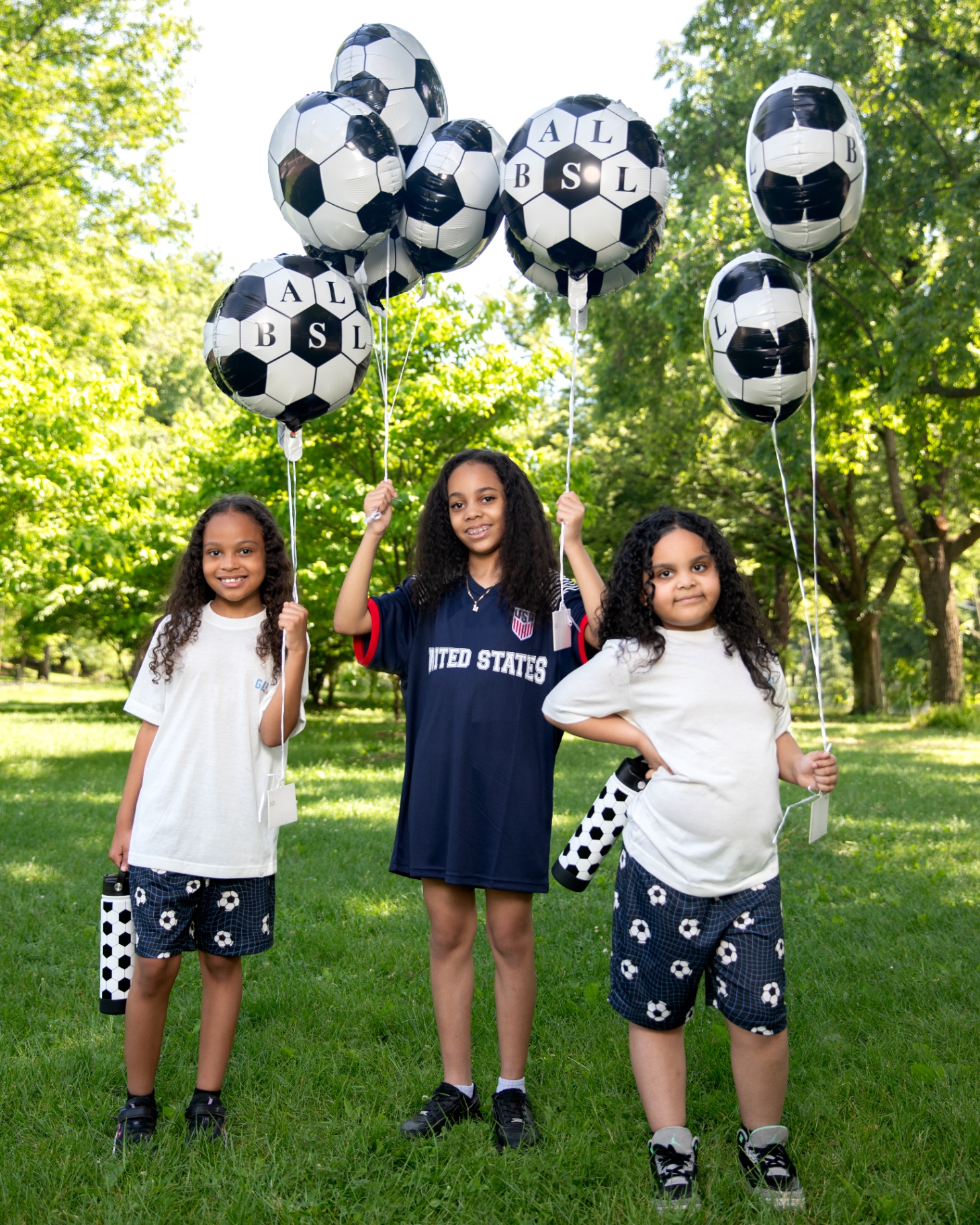 Three kids holding soccer balloons in the park